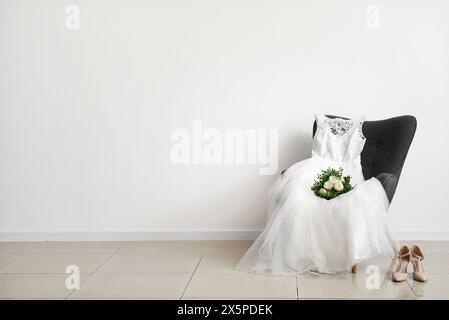 Wedding dress, bridal bouquet on grey chair and wedding shoes on floor in room Stock Photo