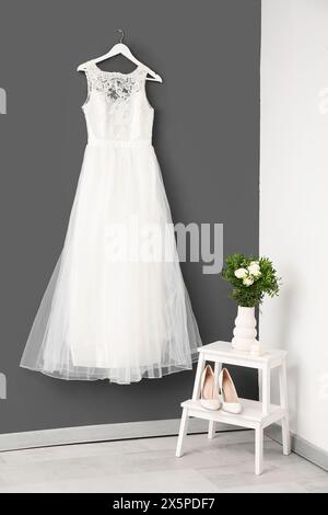 Beautiful wedding dress, shoes and bouquet near grey wall Stock Photo