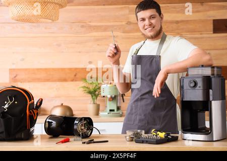Male worker with screwdriver repairing coffee machine in kitchen Stock Photo