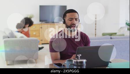 Image of dots moving over happy biracial man working on laptop at home Stock Photo