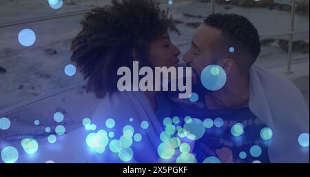 Image of glowing blue spots falling over african american couple embracing each other at beach Stock Photo