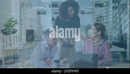 Image of numbers and aerial view of buildings on diverse coworkers discussing reports on laptop Stock Photo