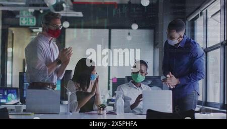 In this image, office colleagues are seen clapping together while wearing face masks Stock Photo