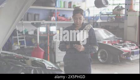 Image of financial data processing over biracial female car mechanic using tablet Stock Photo