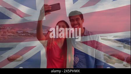 Image of flag of uk flag over happy diverse couple taking selfie by sea Stock Photo