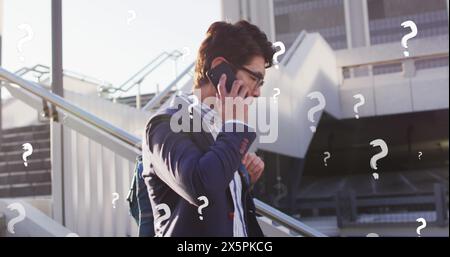 Image of question marks over asian businessman talking on cellphone while moving down steps Stock Photo