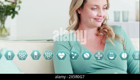 Caucasian pregnant woman sitting, looking at health icons Stock Photo