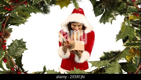 Caucasian woman in Santa costume opening gift, wearing a red hat Stock Photo