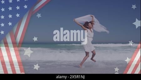 Image of american flag over african american woman raising hands at beach Stock Photo