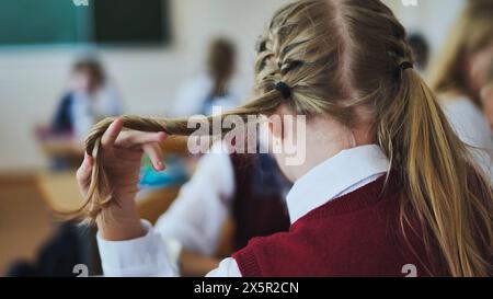 A girl touches a braid of her hair during class. Stock Photo