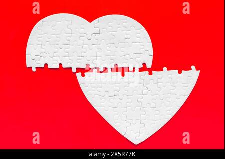 White heart-shaped puzzle, split in half, lying on a bold red background. Separation, longing or incomplete love related concept. Stock Photo