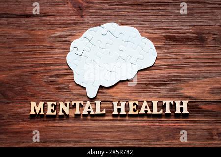 Complete brain-shaped puzzle with the lettering "Mental Health" spelled out in wooden letters on a wooden background. Mental well-being and psychology Stock Photo
