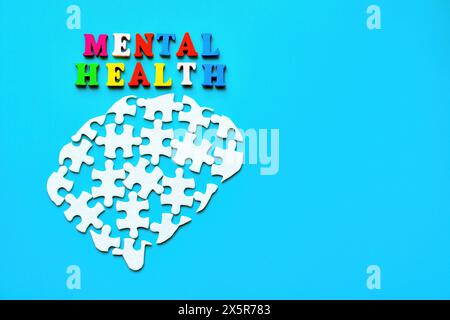 Disassembled brain puzzle on a blue background with the words "Mental Health" spelled out in colorful wooden letters. Stock Photo