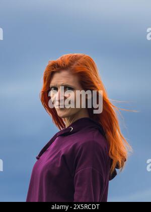 Portrait of redheaded smiling young woman against blue cloud Stock Photo