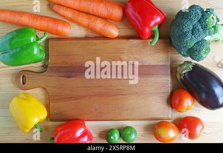 Colorful fresh mixed vegetables surrounding an empty wooden chopping board Stock Photo