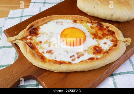Freshly Baked Adjarian Khachapuri, Cheese and Fresh Egg Filled Georgian Bread on wooden Breadboard Stock Photo