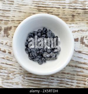 Tumbled close up snowflake obsidian on white wood textured background top view Stock Photo