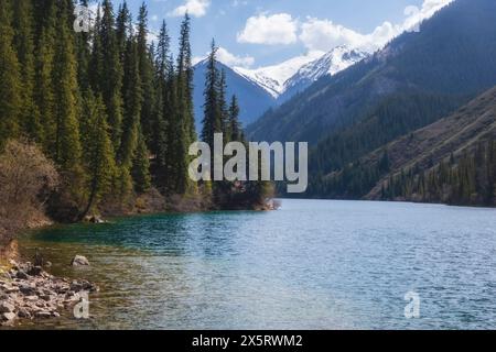 Blue water of a mountain lake in the forest. Kolsai lakes in spring in Kazakhstan. Stock Photo