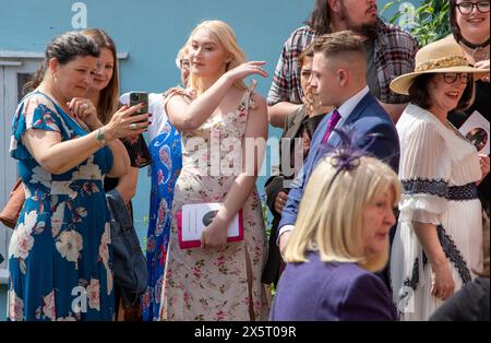 Wedding guests after the ceremony in the Unitarian church Framlingham Suffolk foregather on a sunny day inevitably to look at mobile phones Stock Photo