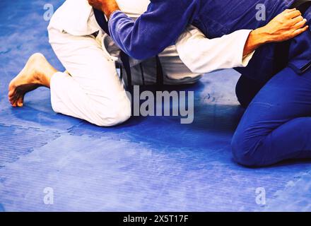 Two men on a blue mat in a Brazilian Jiu-Jitsu training facility. He is focused and practicing the techniques of the martial art Stock Photo