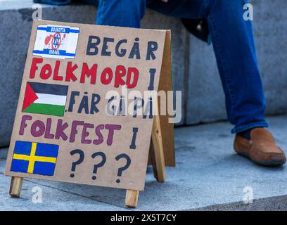 Malmo, Sweden. 11th May, 2024. 11 May 2024, Sweden, Malmö: A poster reading 'Israel is committing genocide in Palestine before going to a national festival in Sweden' is seen during a protest in the city center against Israel's participation in the final of the Eurovision Song Contest (ESC) 2024. The colorful music festival is overshadowed by the Gaza war this year, the police are on alert and are keeping security precautions high. In the world's biggest singing competition under the motto 'United By Music', 26 countries will compete against each other in the final. Photo: Jens Büttner/dpa Cre Stock Photo