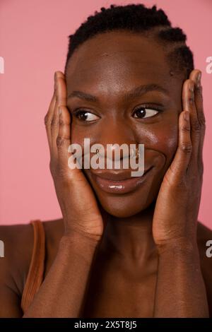 Smiling young woman with face in hands against pink background Stock Photo