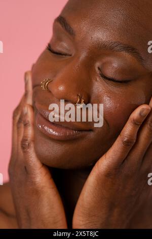Smiling young woman with nose rings touching face Stock Photo
