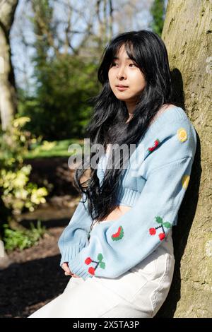Young woman leaning against tree in park Stock Photo