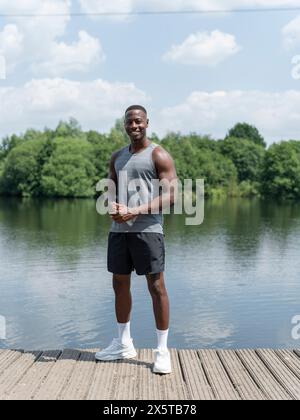 Portrait of smiling muscular man in sports clothing standing by lake Stock Photo
