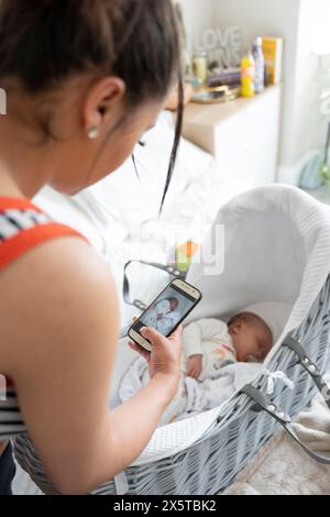 Mother photographing newborn baby girl while sleeping in crib Stock Photo