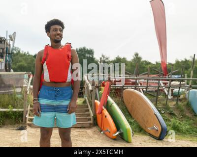 Portrait of young man standing on beach before paddleboarding Stock Photo