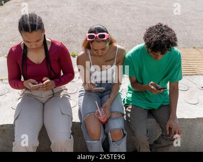 Friends using smart phones while sitting on stone wall Stock Photo