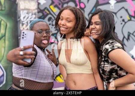 Portrait of three friends talking selfie with smart phone against graffiti wall Stock Photo