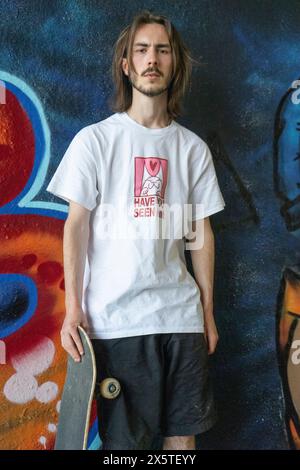 Portrait of young man standing against graffiti wall and holding skateboard Stock Photo