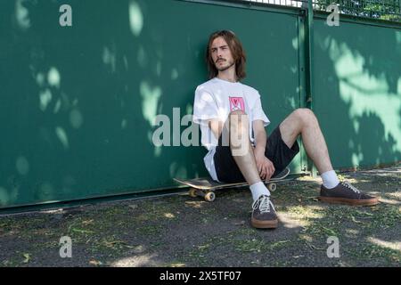 Young man sitting on skateboard in park Stock Photo