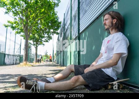 Young man sitting on skateboard outdoors Stock Photo