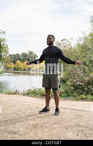 Smiling man exercising with jump rope against trees at park Stock Photo ...