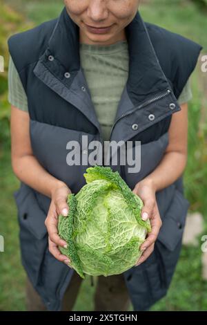 Mid section of woman holding homegrown cabbage in urban garden Stock Photo