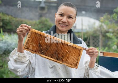 Portrait of smiling female beekeeper holding frame from beehive in urban garden Stock Photo