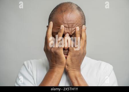 Portrait of man covering head with hands against gray background Stock Photo