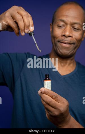 Portrait of man taking medicine with pipette against purple background Stock Photo