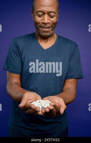Portrait of smiling man holding pills in hands against purple background Stock Photo