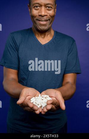 Portrait of smiling man holding pills in hands against purple background Stock Photo