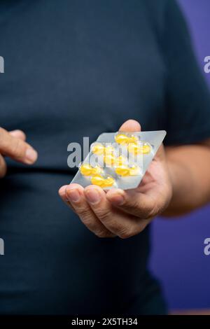 Man holding blister with yellow capsules against purple background Stock Photo