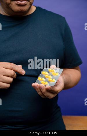 Man holding blister with yellow capsules against purple background Stock Photo