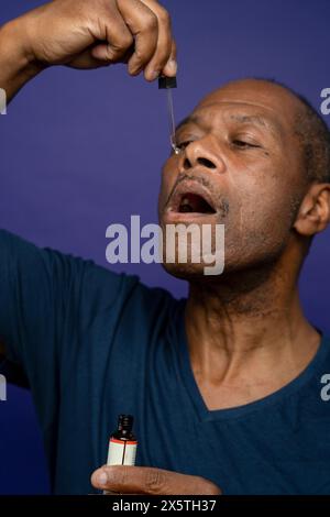 Man taking medicine with pipette against purple background Stock Photo