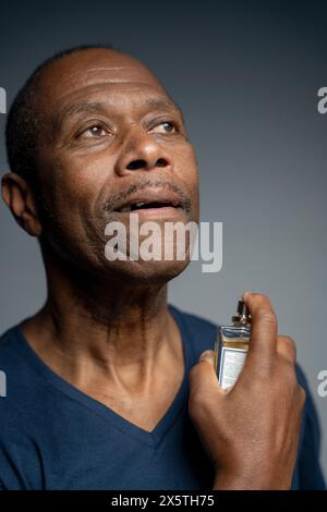 Portrait of man putting on perfume against gray background Stock Photo