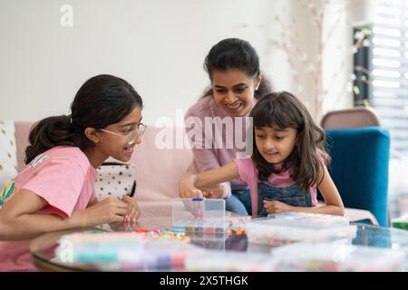 Mother with daughters playing with beads in living room Stock Photo