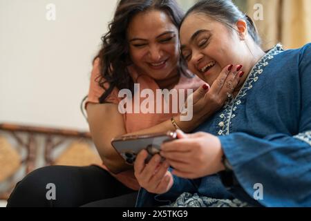 Woman with down syndrome daughter using smart phone at home Stock Photo