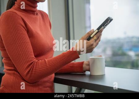 Midsection of woman using smart phone in office kitchen Stock Photo